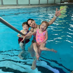 Instructor with two children in a swimming pool, showcasing fun and engagement in swimming lessons at Aqua Life Swim Academy.