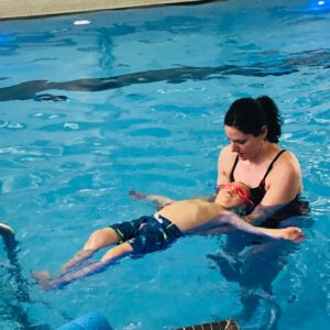 Instructor supporting child in swimming lesson, demonstrating safety and comfort in water at Aqua Life Swim Academy.