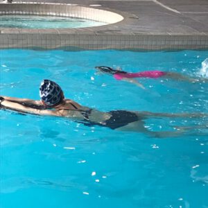 Two children swimming in a pool, one wearing a swim cap and focusing on technique, while the other swims nearby, illustrating personalized swimming lessons at Aqua Life Swim Academy.