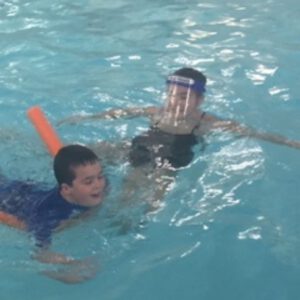 Child learning to swim with instructor using a pool noodle in Aqua Life Swim Academy's safe and engaging environment.