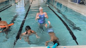 Swimming instructor engaging with children in a pool during a lesson, emphasizing personalized coaching and enjoyment at Aqua Life Swim Academy.