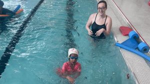 Child learning to swim in pool with instructor, both smiling, showcasing personalized swimming lessons at Aqua Life Swim Academy.