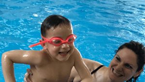 Happy child in pink swim goggles enjoying a swimming lesson with a smiling instructor in a pool, highlighting personalized attention at Aqua Life Swim Academy.