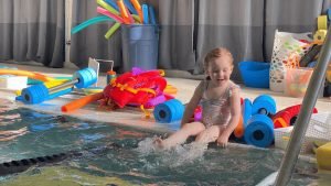 Young child splashing in a pool surrounded by colorful swim toys, illustrating the fun and engaging atmosphere of Aqua Life Swim Academy's swimming lessons.