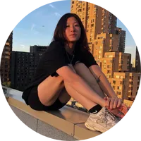 Person sitting on a ledge in an urban setting, wearing casual athletic clothing, showcasing a relaxed pose against a backdrop of tall buildings and a clear sky, reflecting a confident and carefree attitude.